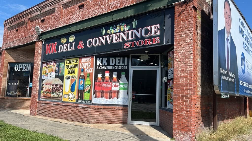 Full view of the KK Deli storefront with its awning sign and window displays.